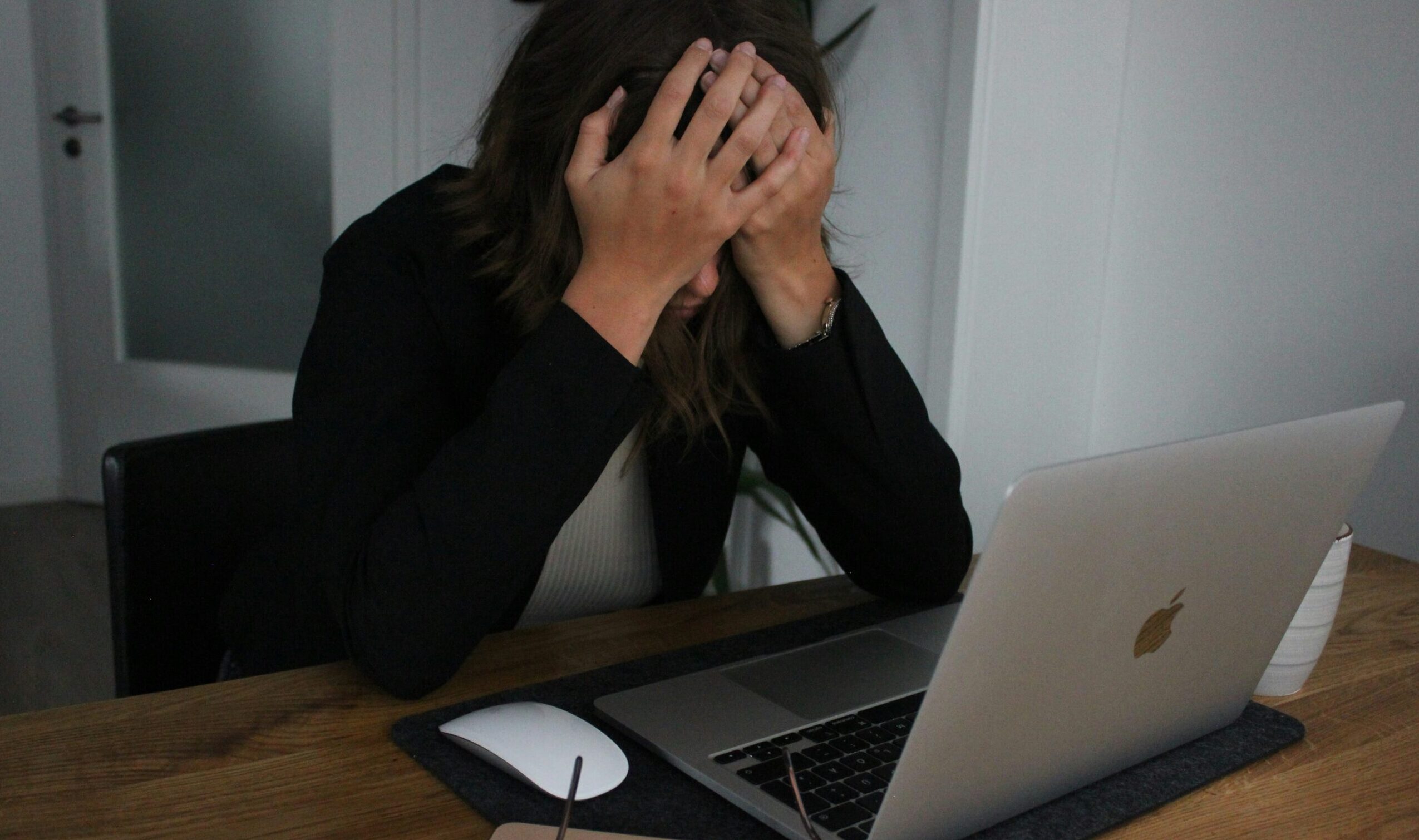 A woman feeling stressed with her head in her hands looking at her computer screen.